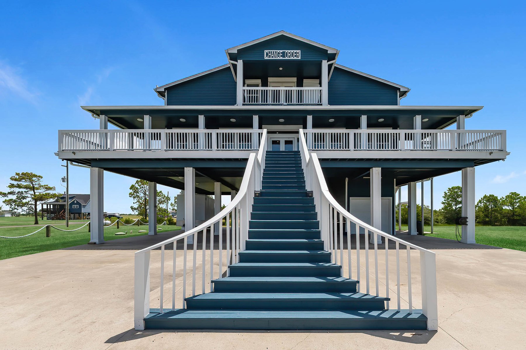 Raised blue coastal home with a grand front staircase and wraparound porches