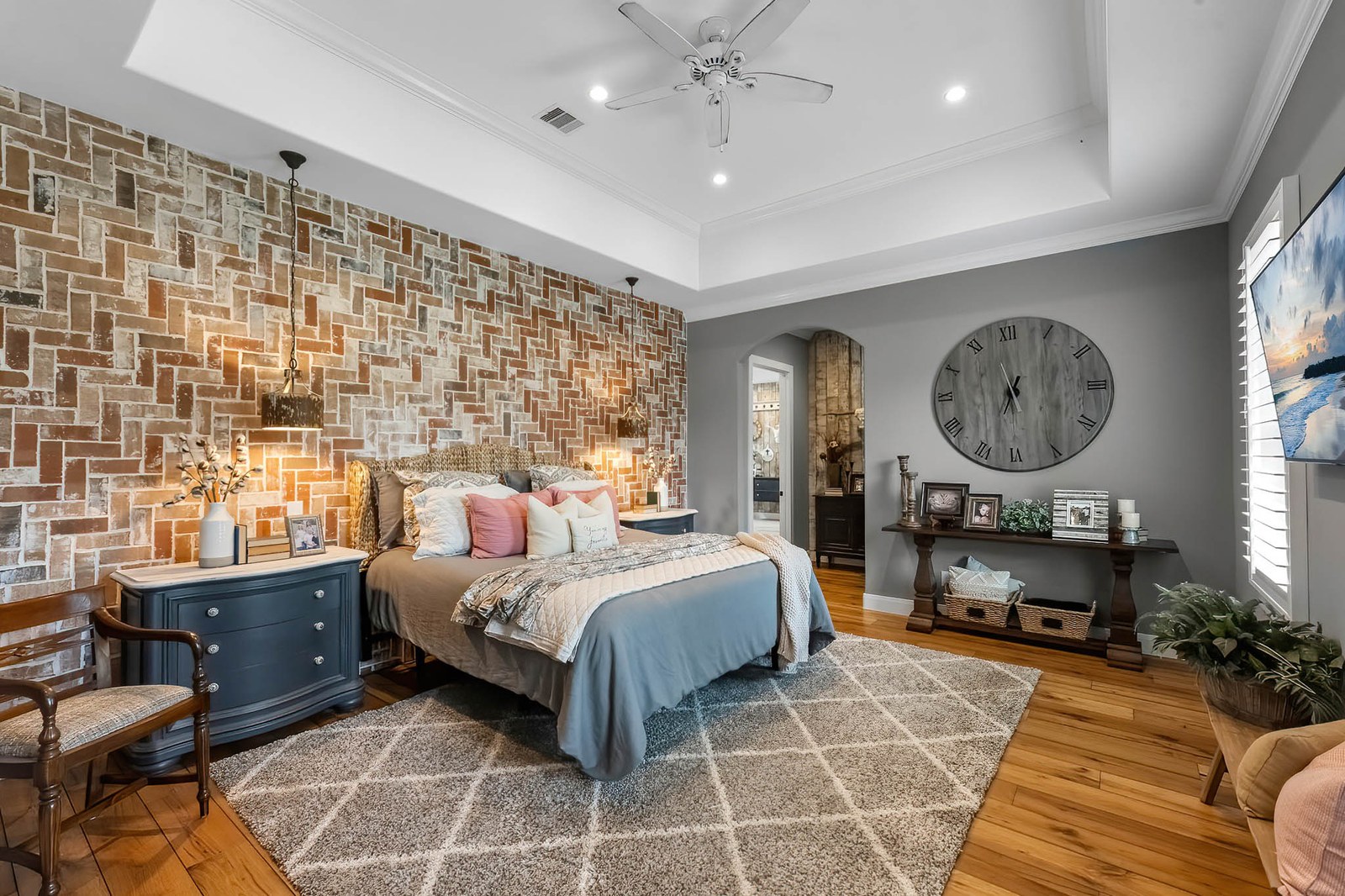 Bedroom with a herringbone brick accent wall, tray ceiling and oversized clock