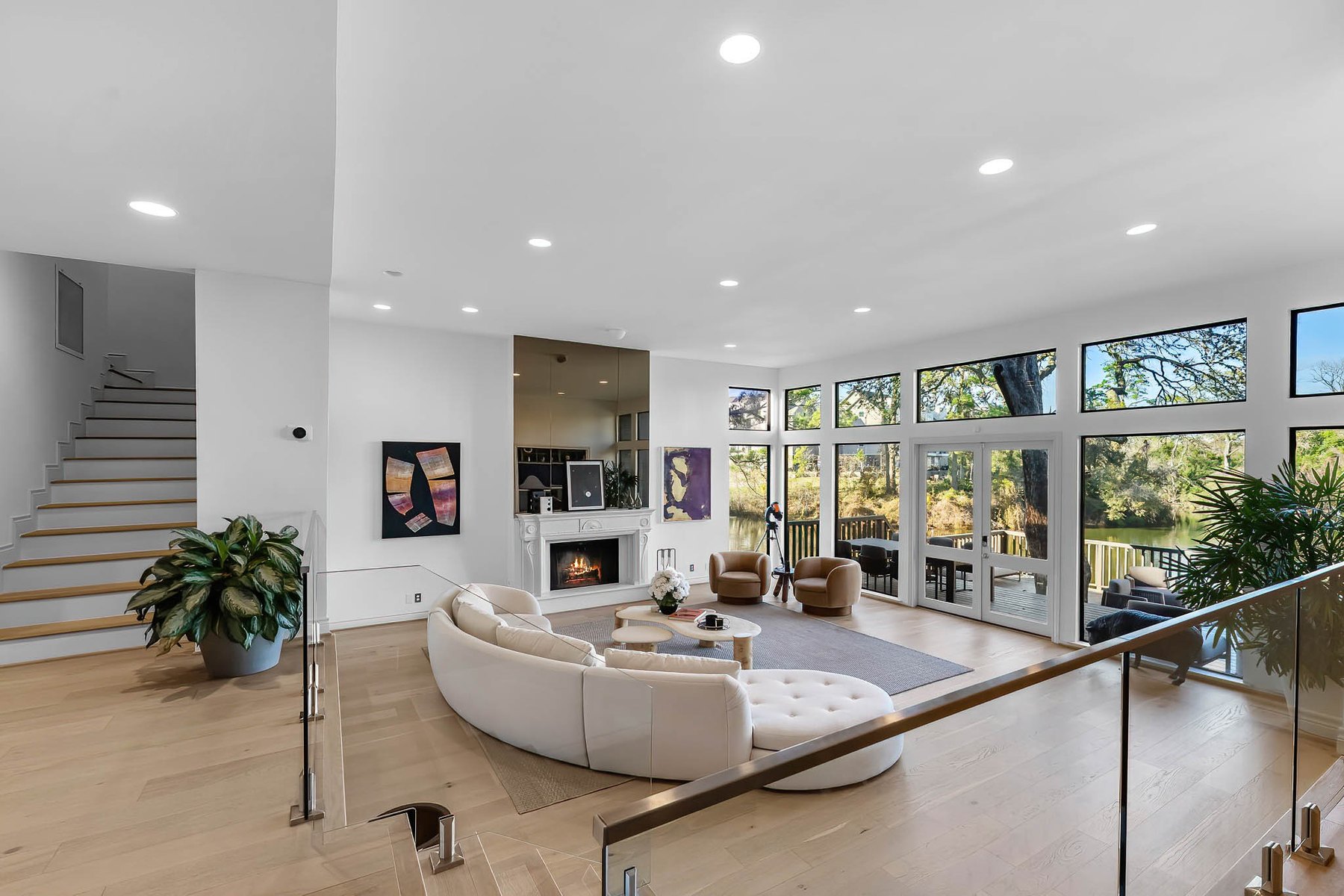 Open living room with a curved white sofa, glass stair rail and a wall of windows