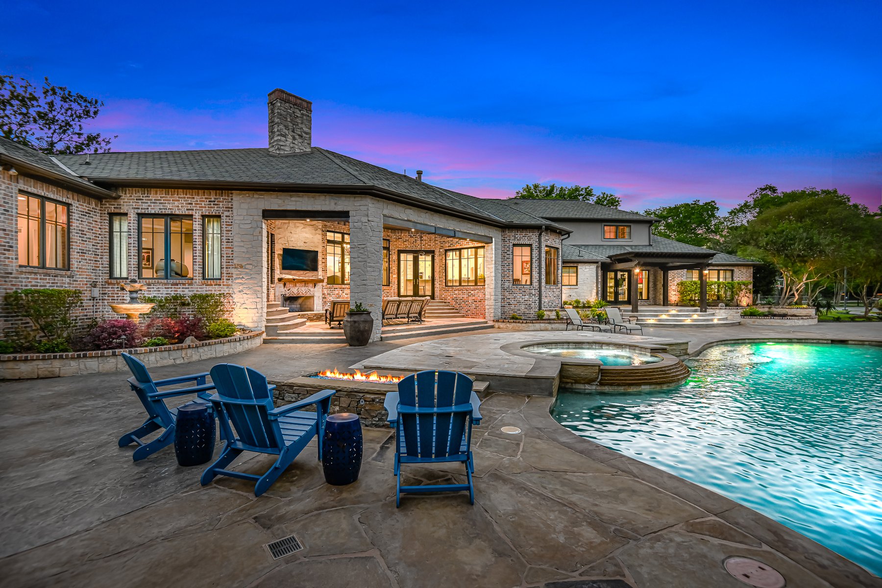 Stone home with a pool and blue Adirondack chairs at dusk
