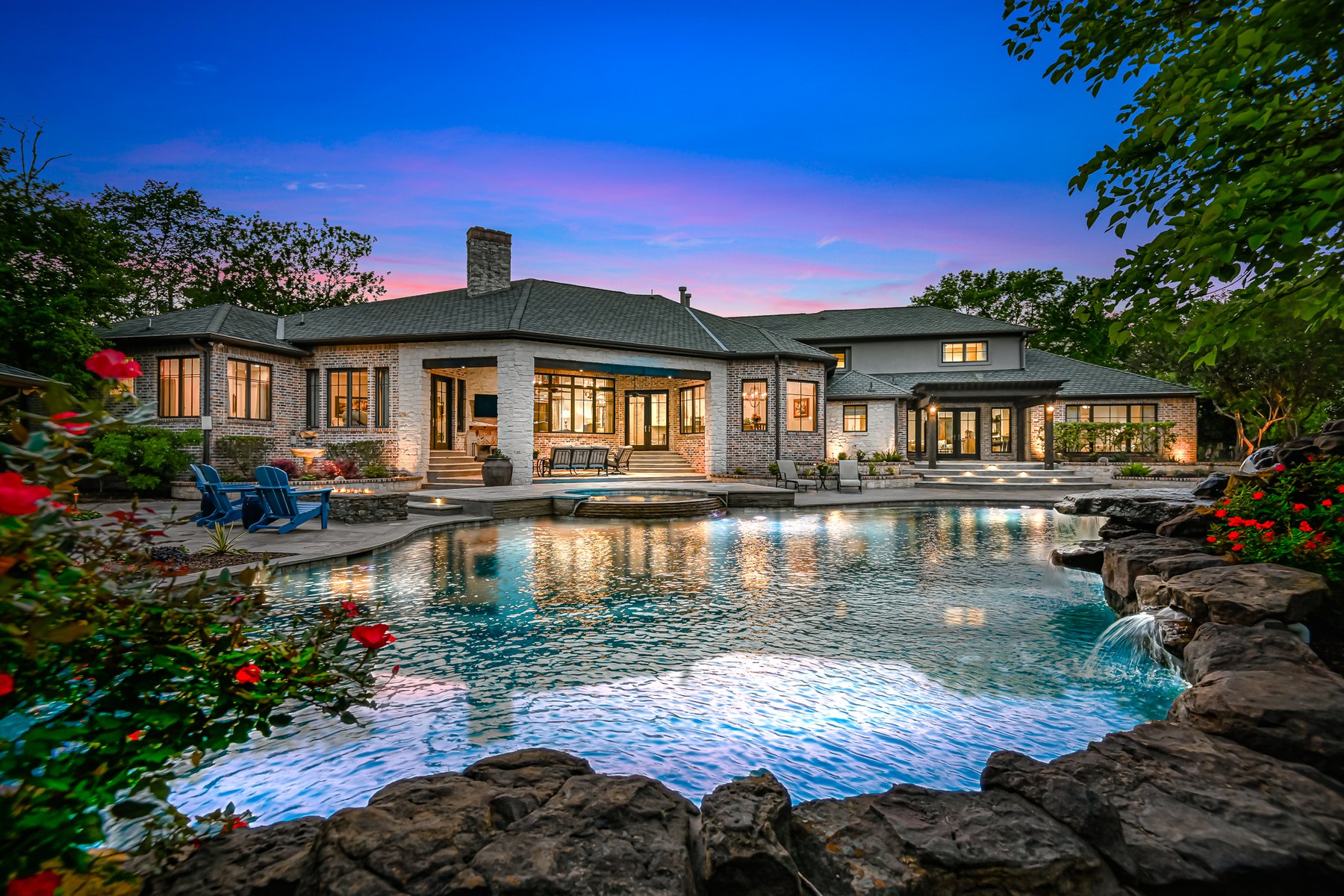 Rock-edged resort pool in front of a home at dusk
