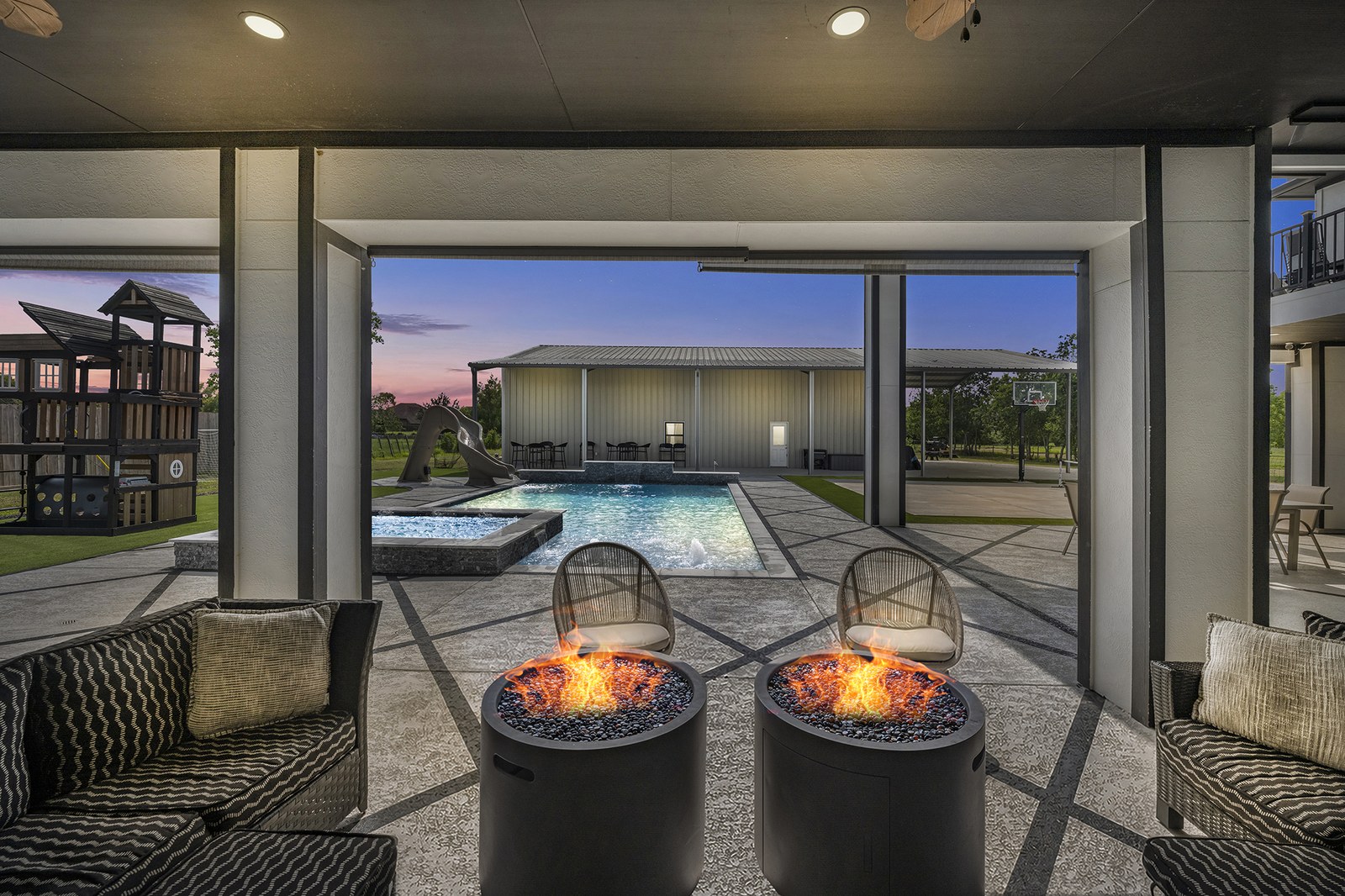 Virtual twilight view from a covered patio with twin fire pits looking out to a lit pool and spa