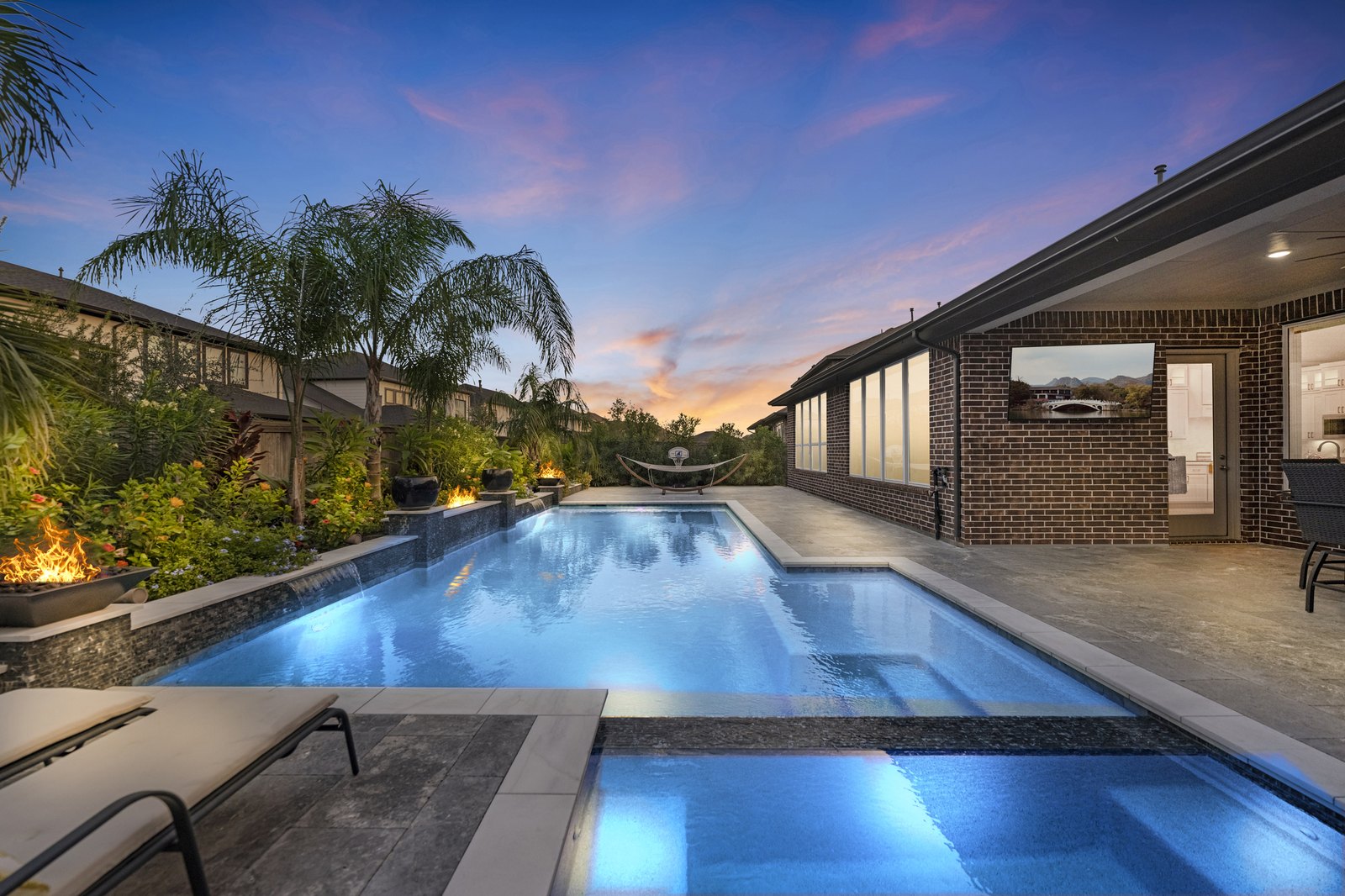 Virtual twilight of a long pool and covered patio with lit fire bowls